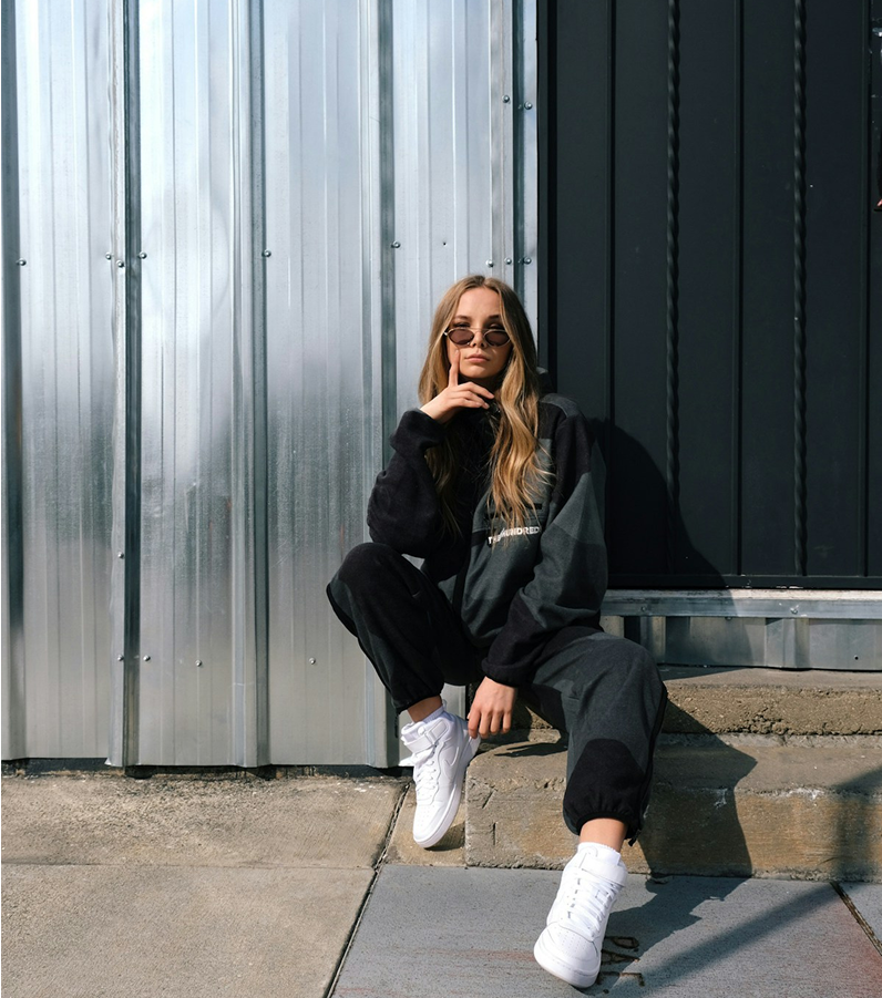 Person wearing a black outfit with white sneakers sitting on steps against a metallic wall.
